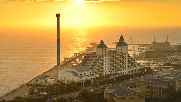 A coastal hotel with a prominent tower, a large building with multiple towers, and a pier extending into the water.