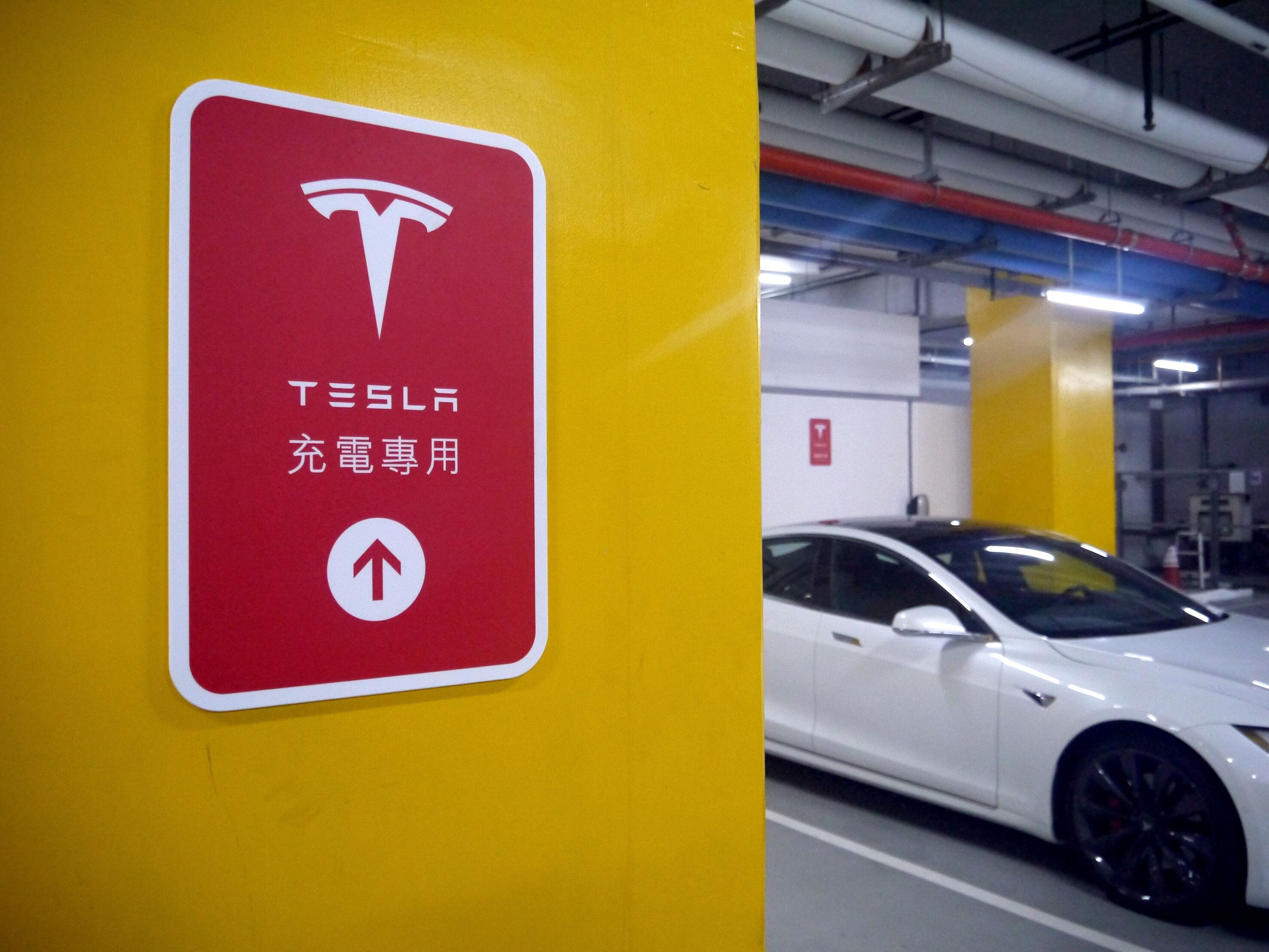 Un panneau indiquant une borne de recharge Tesla, sur un mur jaune dans un parking souterrain.