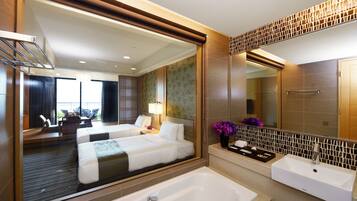 A modern hotel room with a large bed, a separate bathroom, a balcony, and a view of the city.