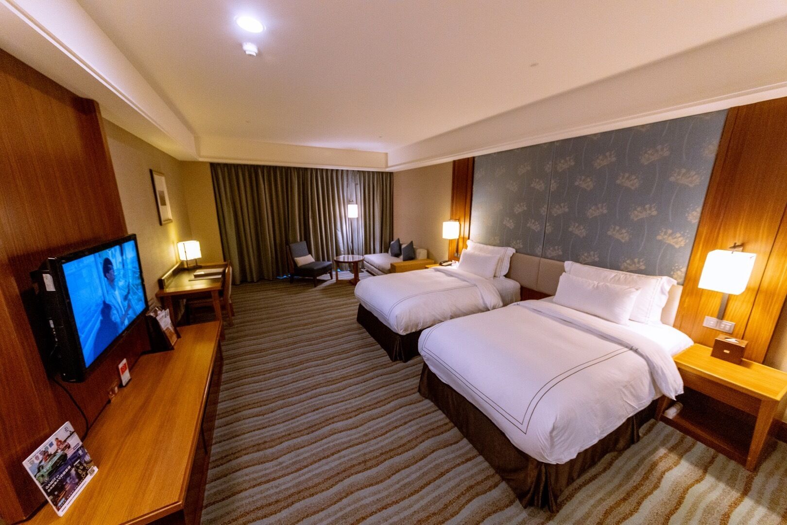 A hotel room with two beds, a TV, a desk, and a chair.