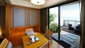 A hotel room with a dining table set for tea, a view of the sea, and a balcony with outdoor seating.