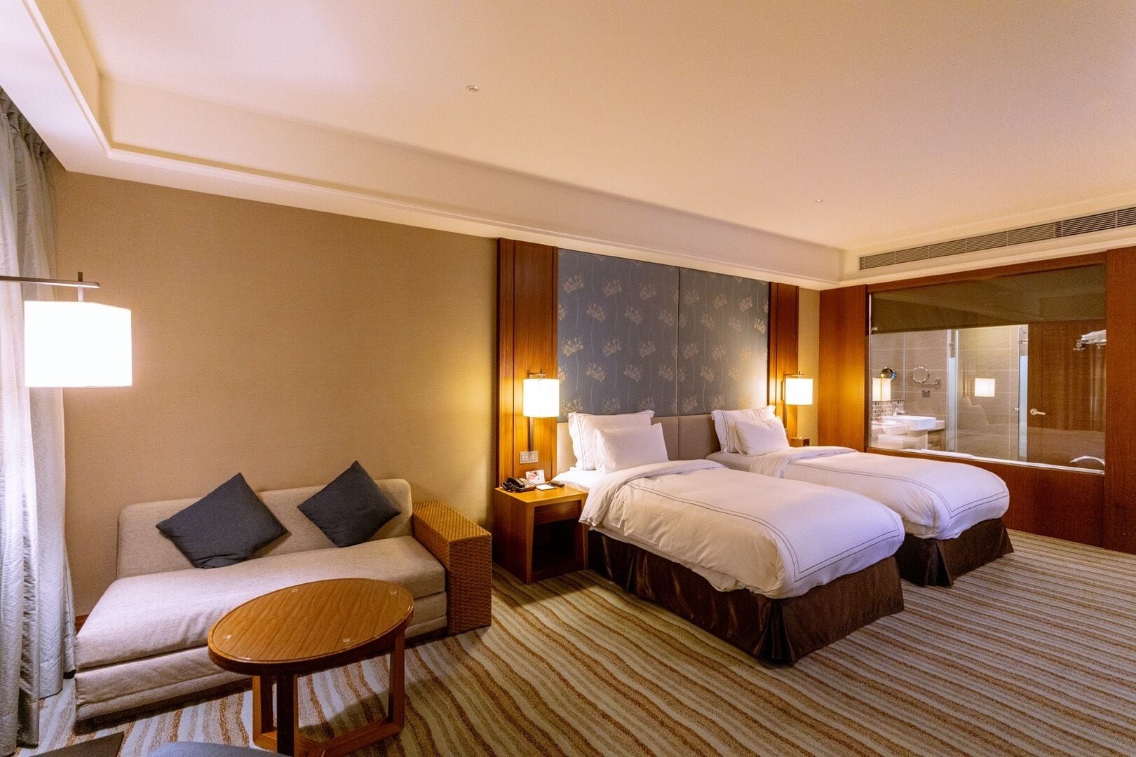 Una habitación de hotel con dos camas, un sofá, una mesita y un espejo grande.