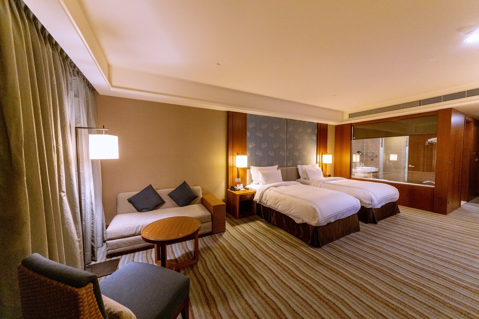 Een hotelkamer met een bank, twee eenpersoonsbedden, een klein rond tafeltje en een stoel.