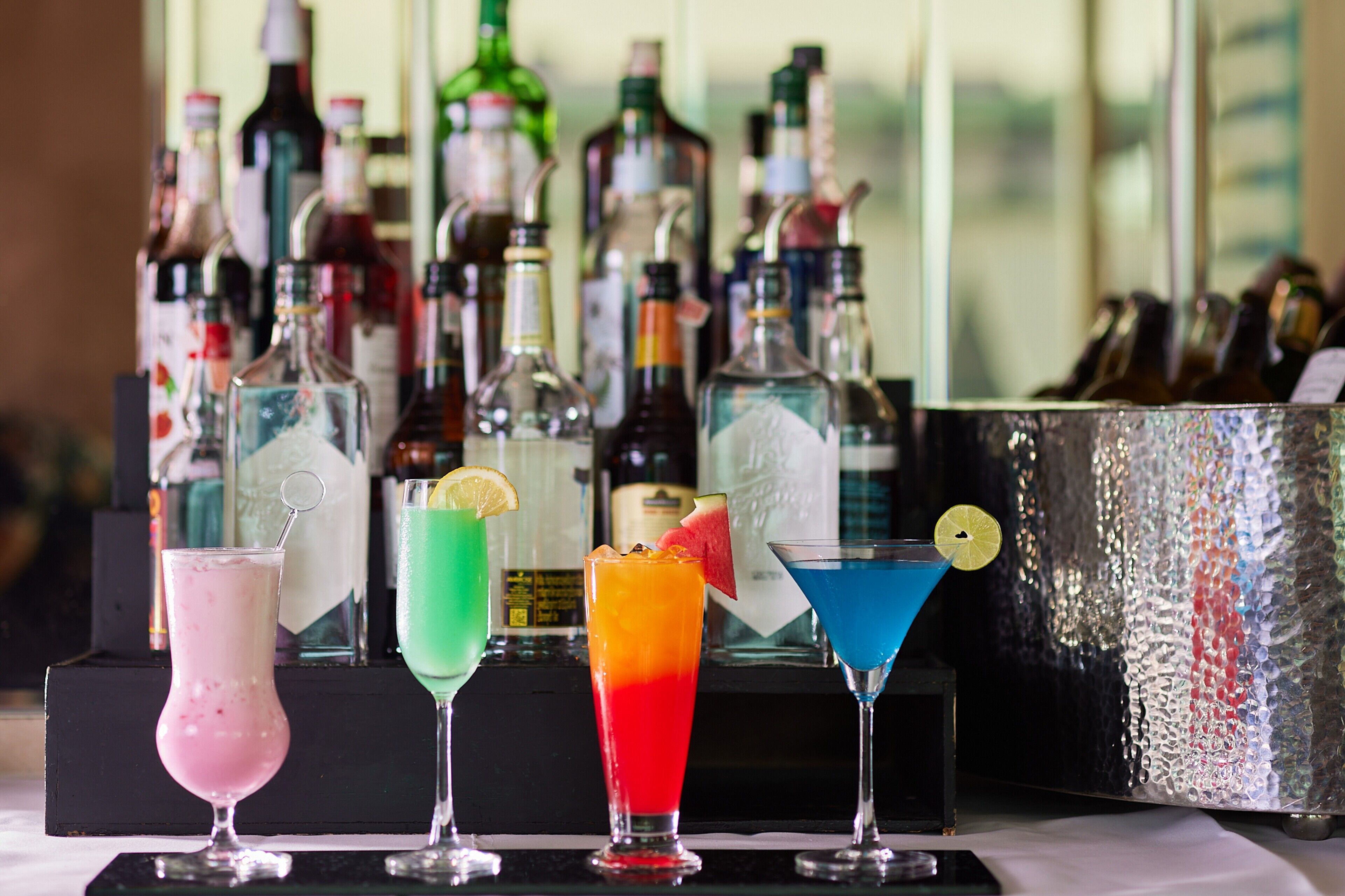 Zona de bar con coloridos cócteles y una selección de botellas de licor al fondo.