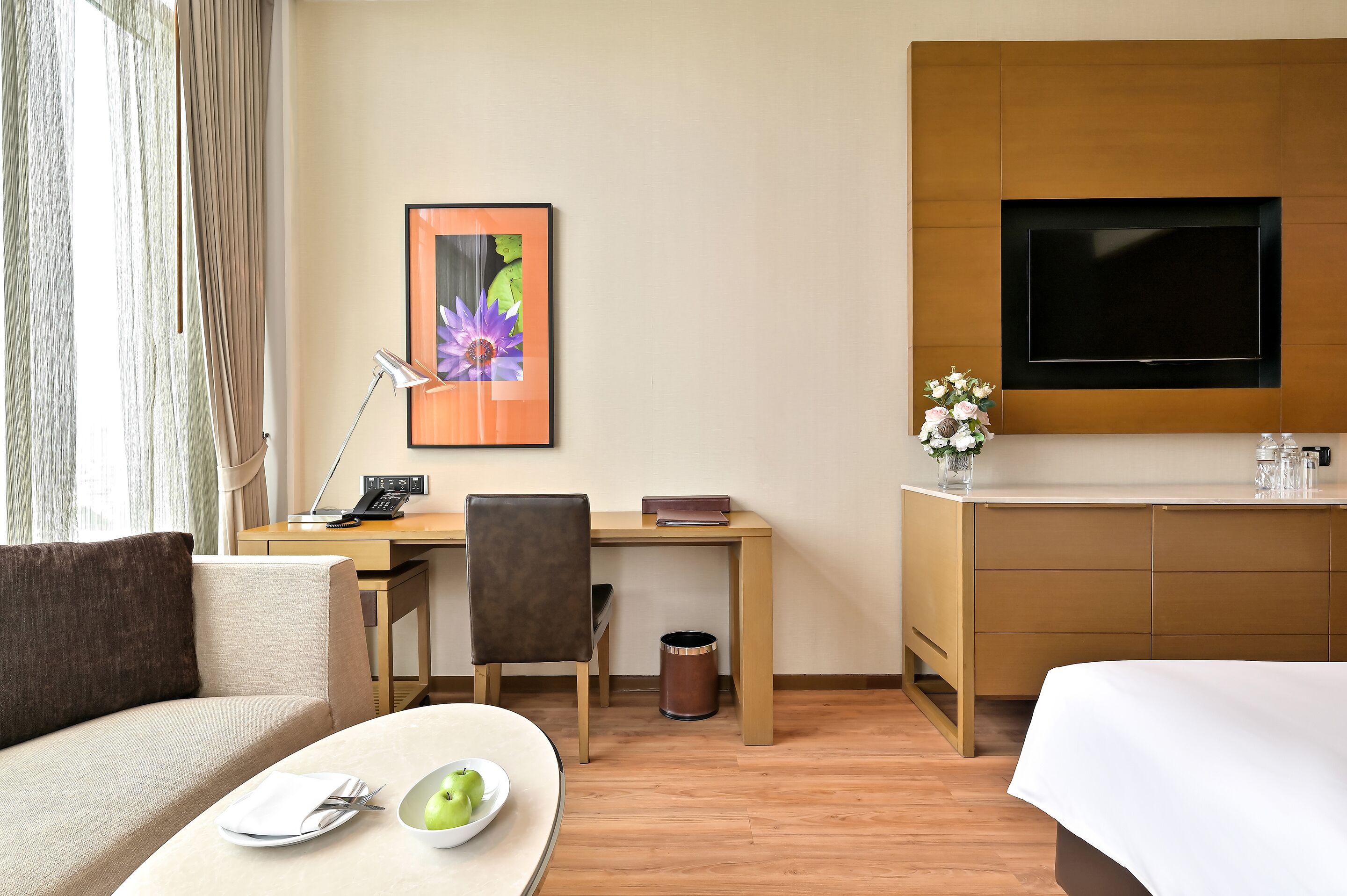 Habitación de hotel con sofá, una mesa de comedor con un frutero, escritorio con lámpara, televisión y minibar.
