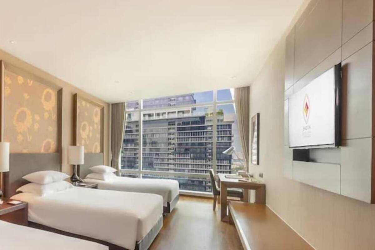 Een hotelkamer met twee bedden, een bureau, een televisie en een groot raam met uitzicht op de stad.