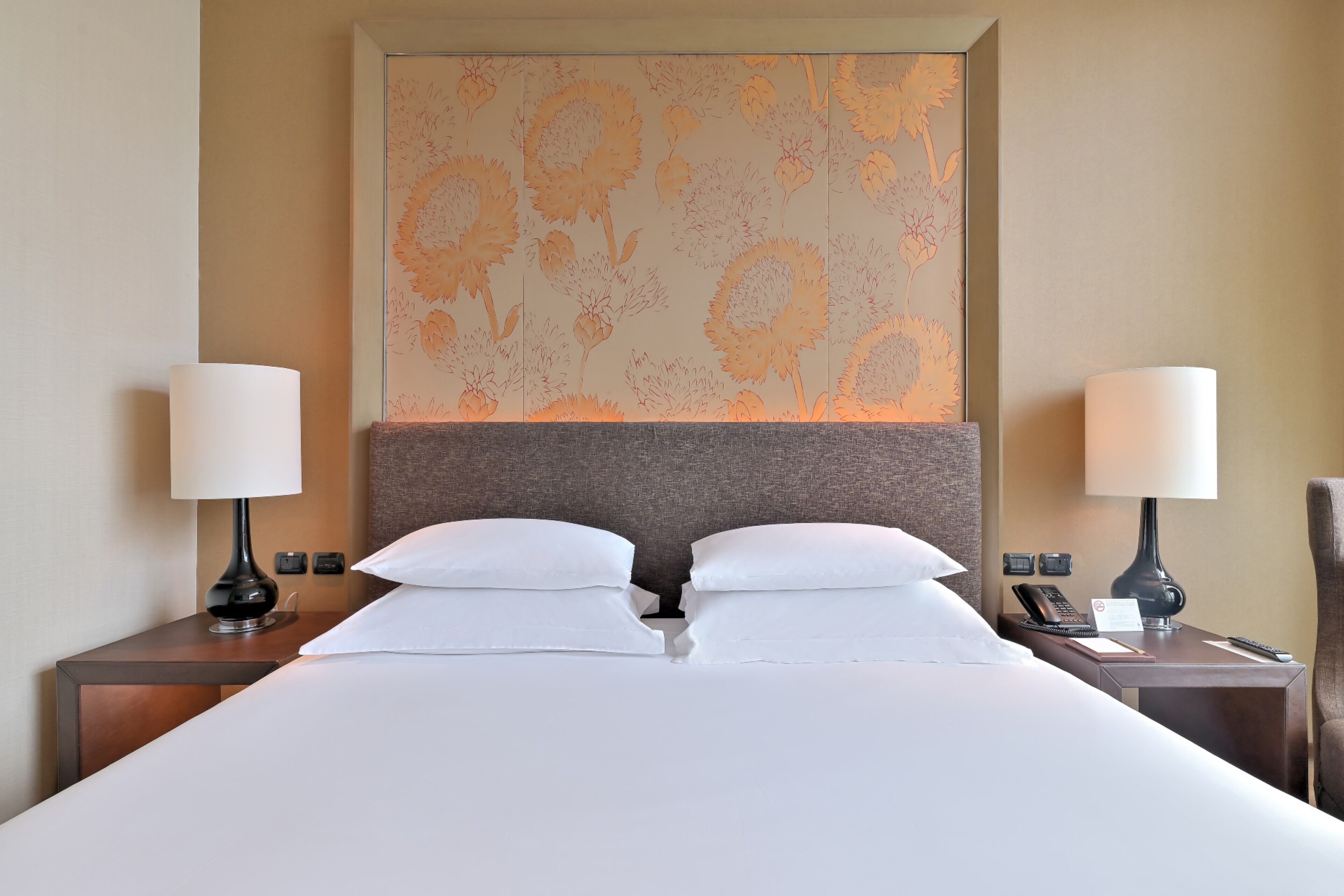 A hotel room with a large bed, two bedside tables with lamps, a wall-mounted telephone, and a decorative panel above the bed.