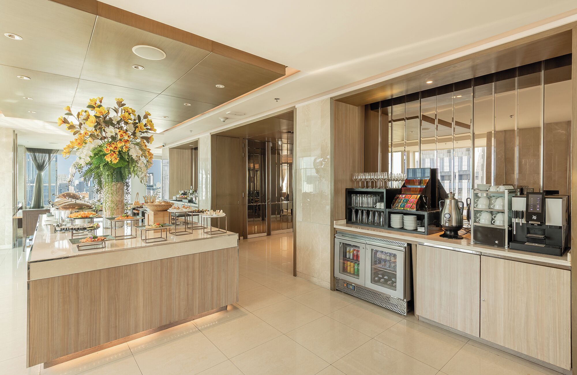 Un hall d’hôtel moderne doté d’un comptoir d’accueil central, d’un espace dédié aux boissons chaudes et offrant une vue sur le paysage urbain grâce à de grandes fenêtres.