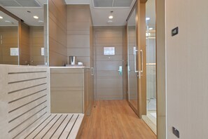 A modern hotel corridor with a wooden floor, a reception desk, and a glass door leading to a shower area.