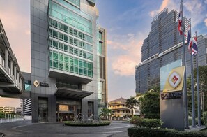 A modern building with a glass facade, a fountain in the courtyard, and flags. - Eastin Grand Hotel Sathorn Bangkok (Bangkok)