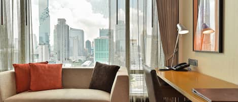 Una habitación de hotel moderna con vista a la ciudad, un sofá, un escritorio y una mesa con manzanas.