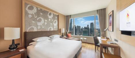 Ein Hotelzimmer mit einem großen Bett, einem Schreibtisch, einem Stuhl, Blick auf die Stadt und einer Wand mit einem Blumenmuster.