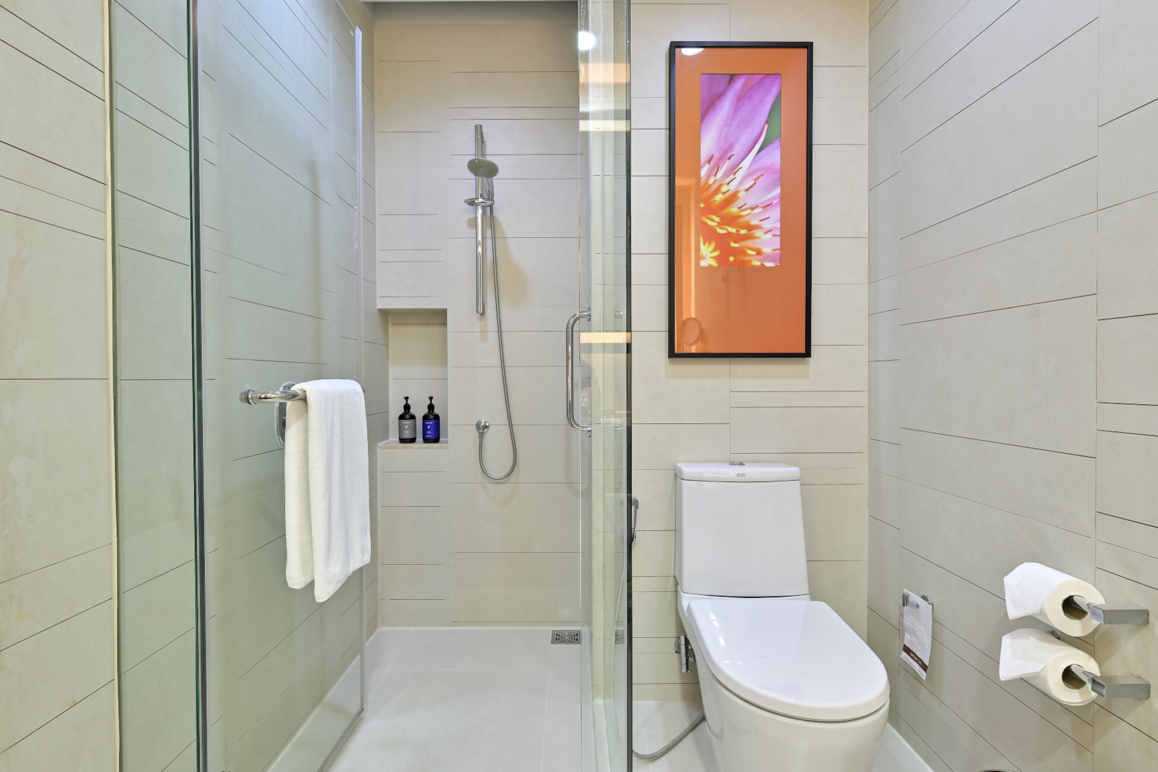 A modern bathroom with a glass-enclosed shower, a white toilet, and a framed floral artwork on the wall.