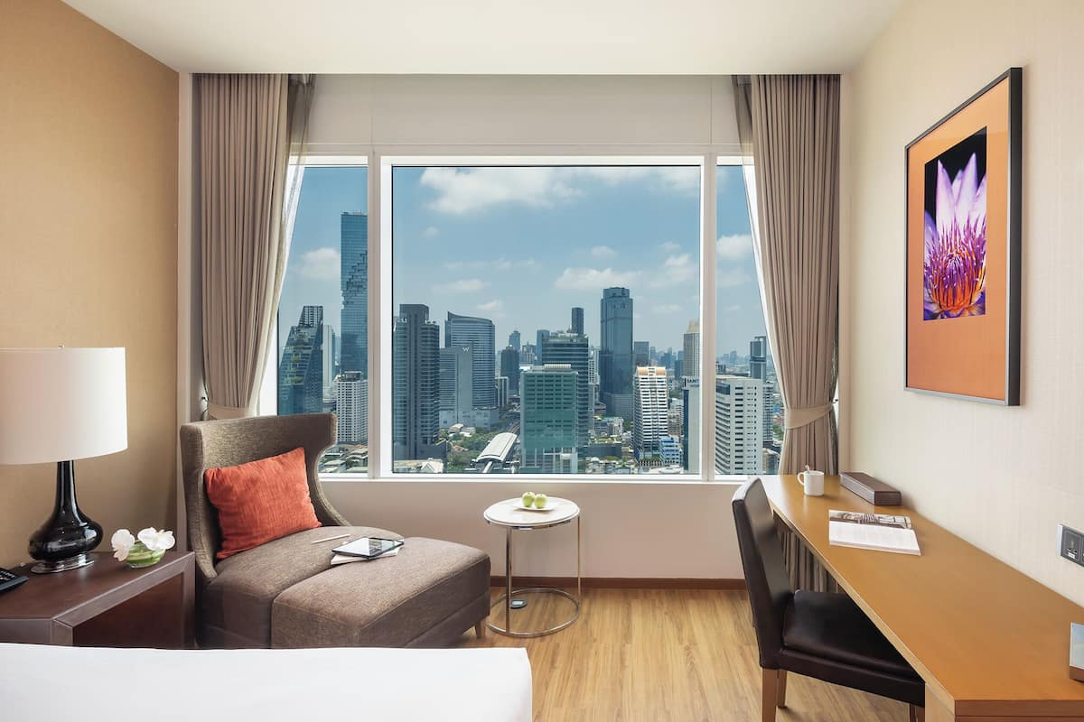 Een hotelkamer met een groot raam, een bed, een bureau en een stoel.