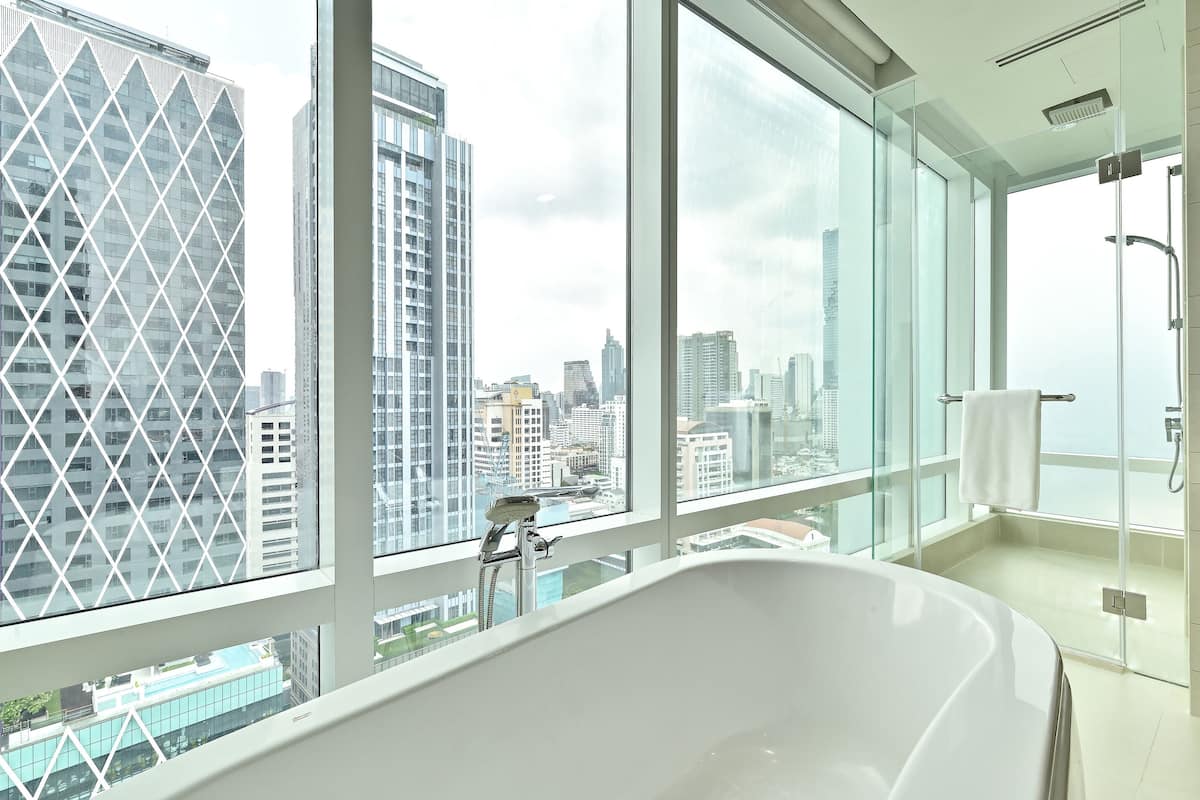 Een moderne badkamer met een ruim bad, een douchecabine van glas en uitzicht op de stad door grote ramen.