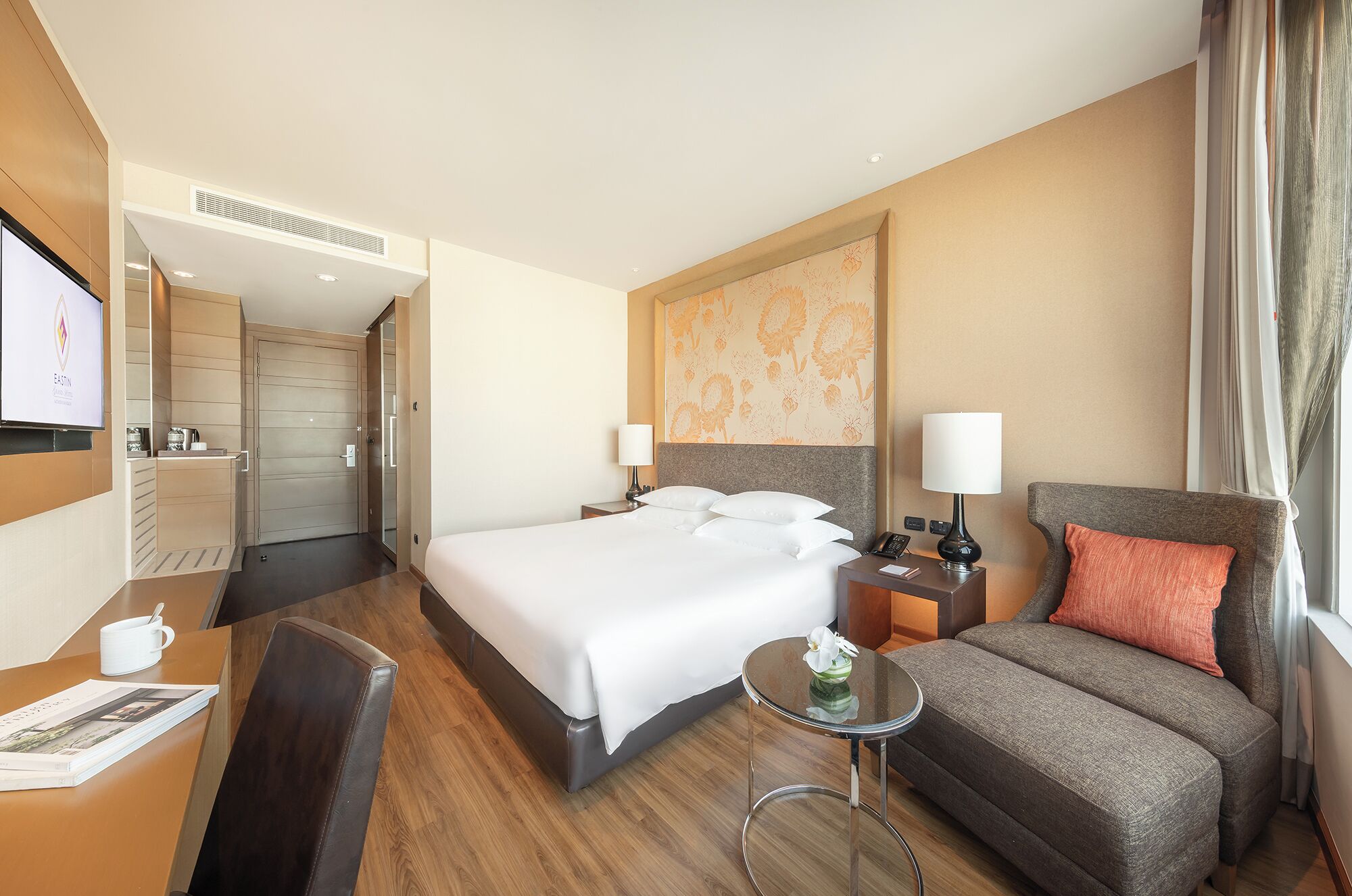 A hotel room with a bed, a desk, a chair, a sofa, and a TV.