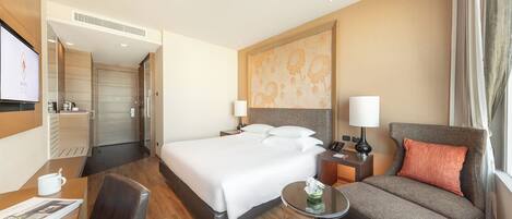 A hotel room with a bed, a desk, a chair, a sofa, and a TV.