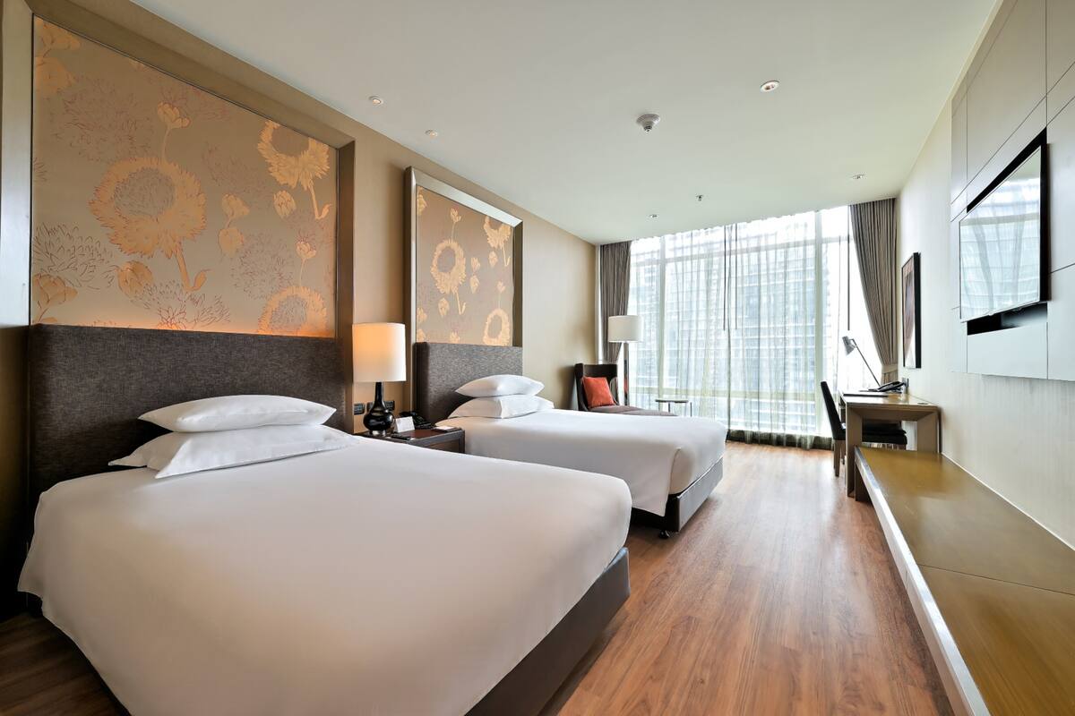 Een hotelkamer met twee bedden, een bureau, een stoel, een televisie en een groot raam met gordijnen.