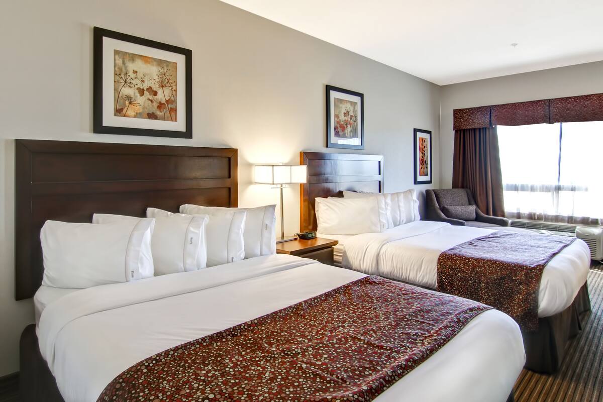 A hotel room with two beds, a desk, a chair, and artwork on the walls.