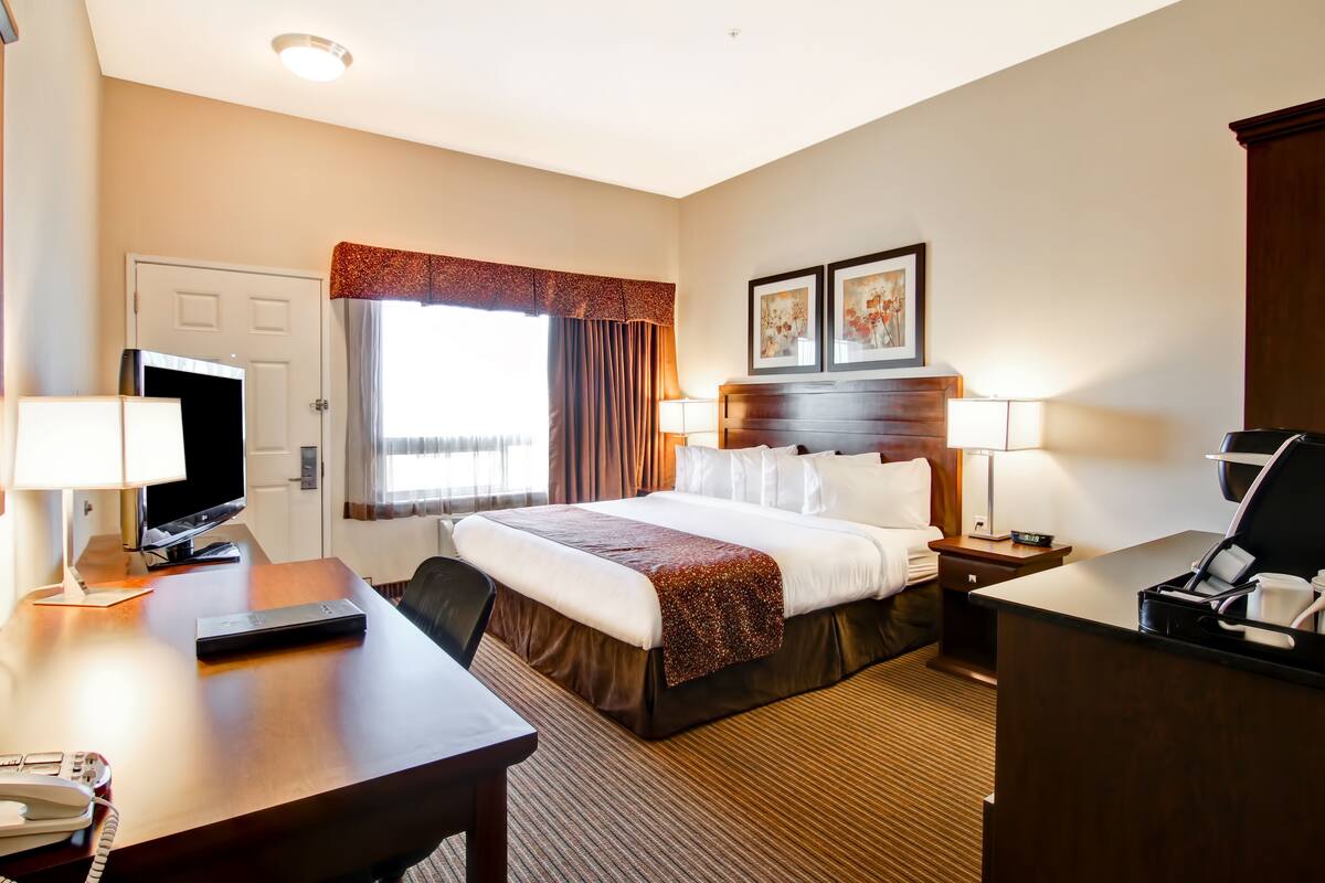 A hotel room with a bed, desk, TV, and a window with curtains.