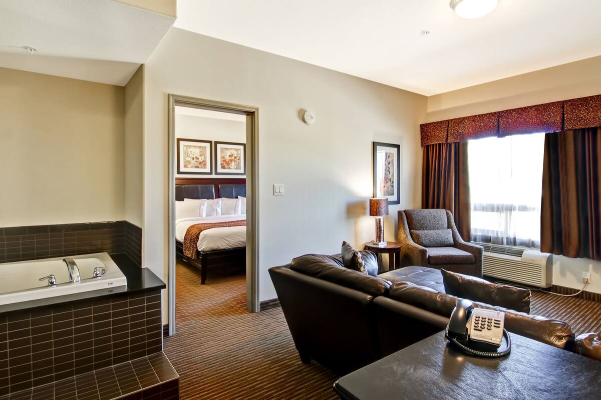 A hotel room with a bathroom, a bed, a sofa, a table with a telephone, and a window with curtains.