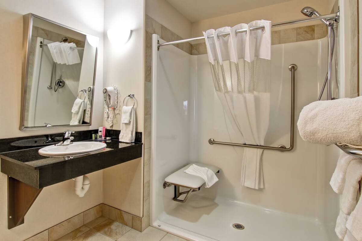 A bathroom with a glass-enclosed shower, a sink with a black countertop, and a mirror.