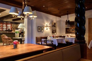 Tunnelmallinen ravintola, jossa on puupöydät ja -tuolit, baarialue sekä seinään kiinnitetyt valaisimet.