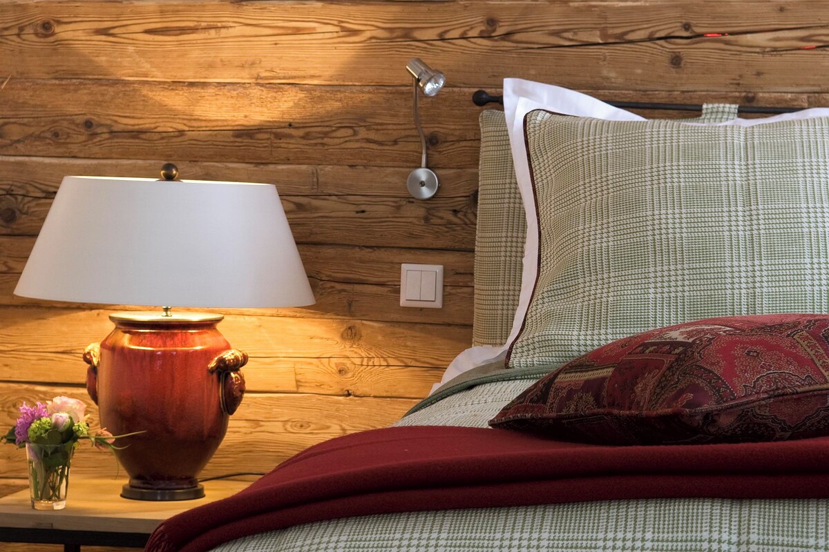 A wooden wall, a lamp, a bed with pillows, and a vase with flowers.