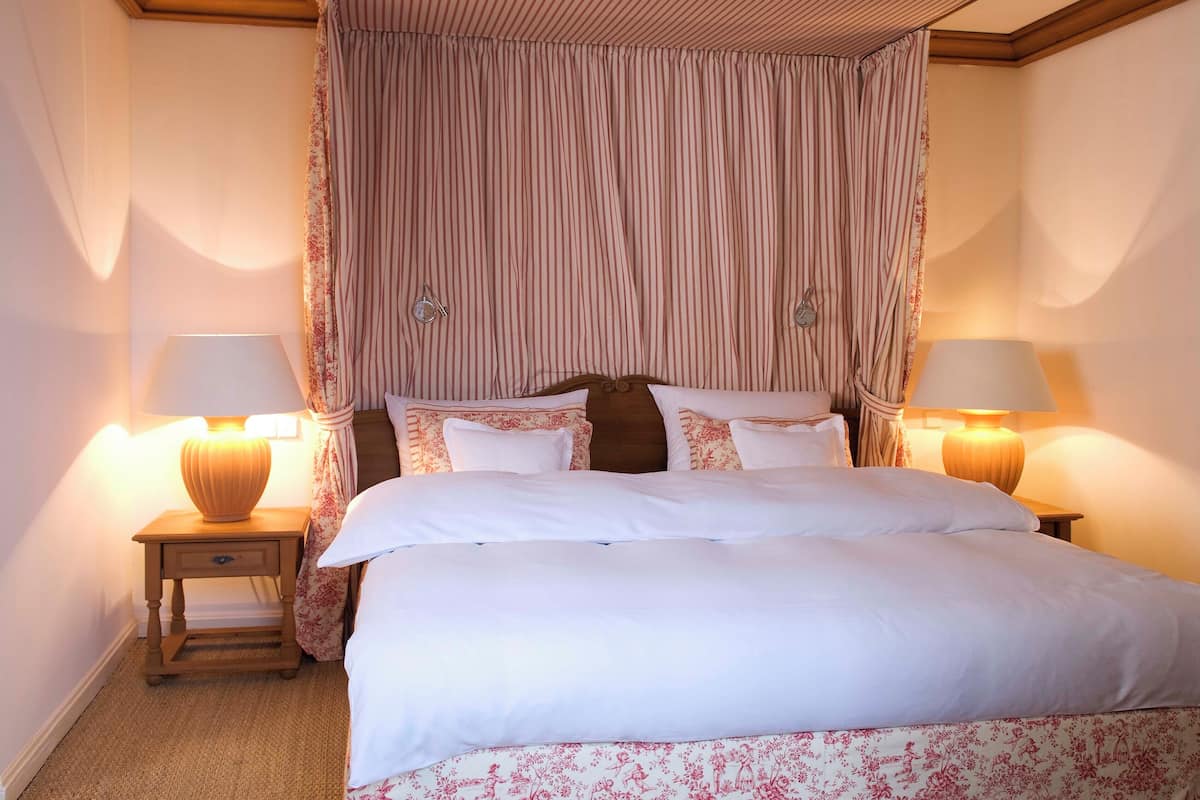 Un lit bien fait, avec du linge de lit blanc, deux lampes de chevet et un baldaquin à rayures.
