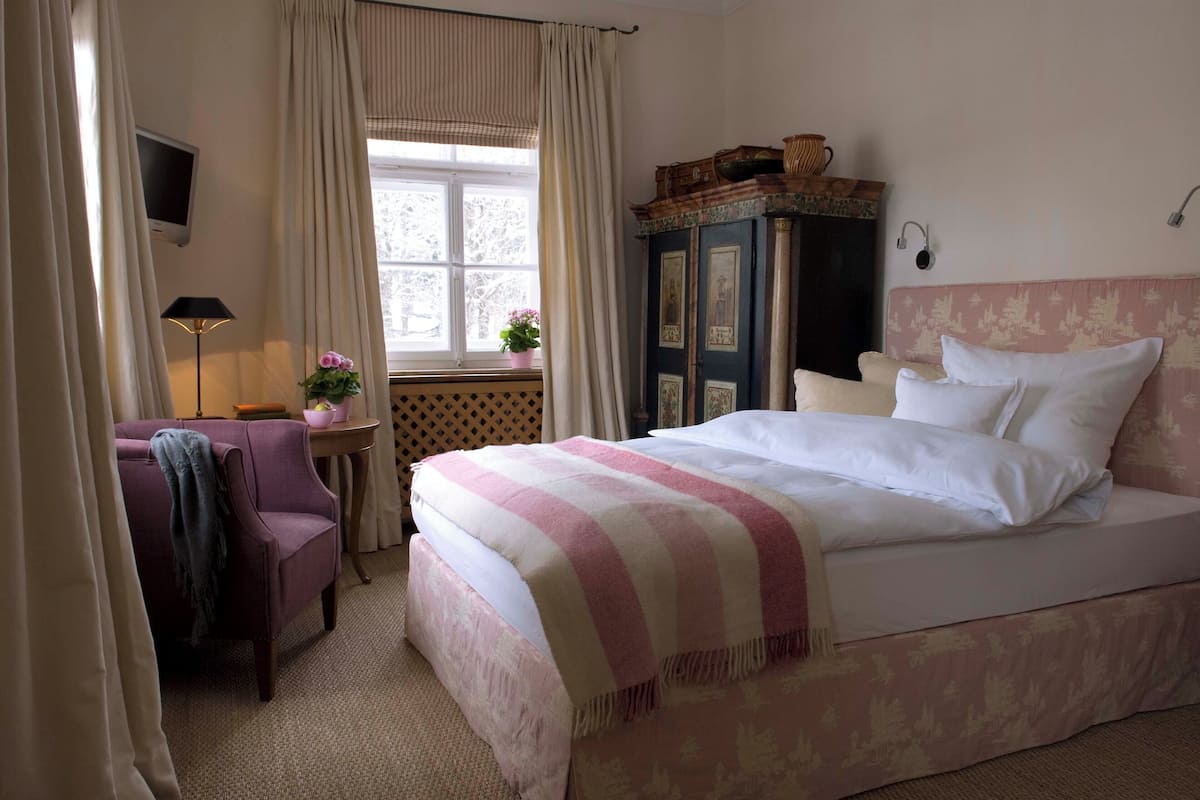 Une chambre à coucher comprenant un lit, un bureau, une chaise, une armoire et une fenêtre avec des rideaux.