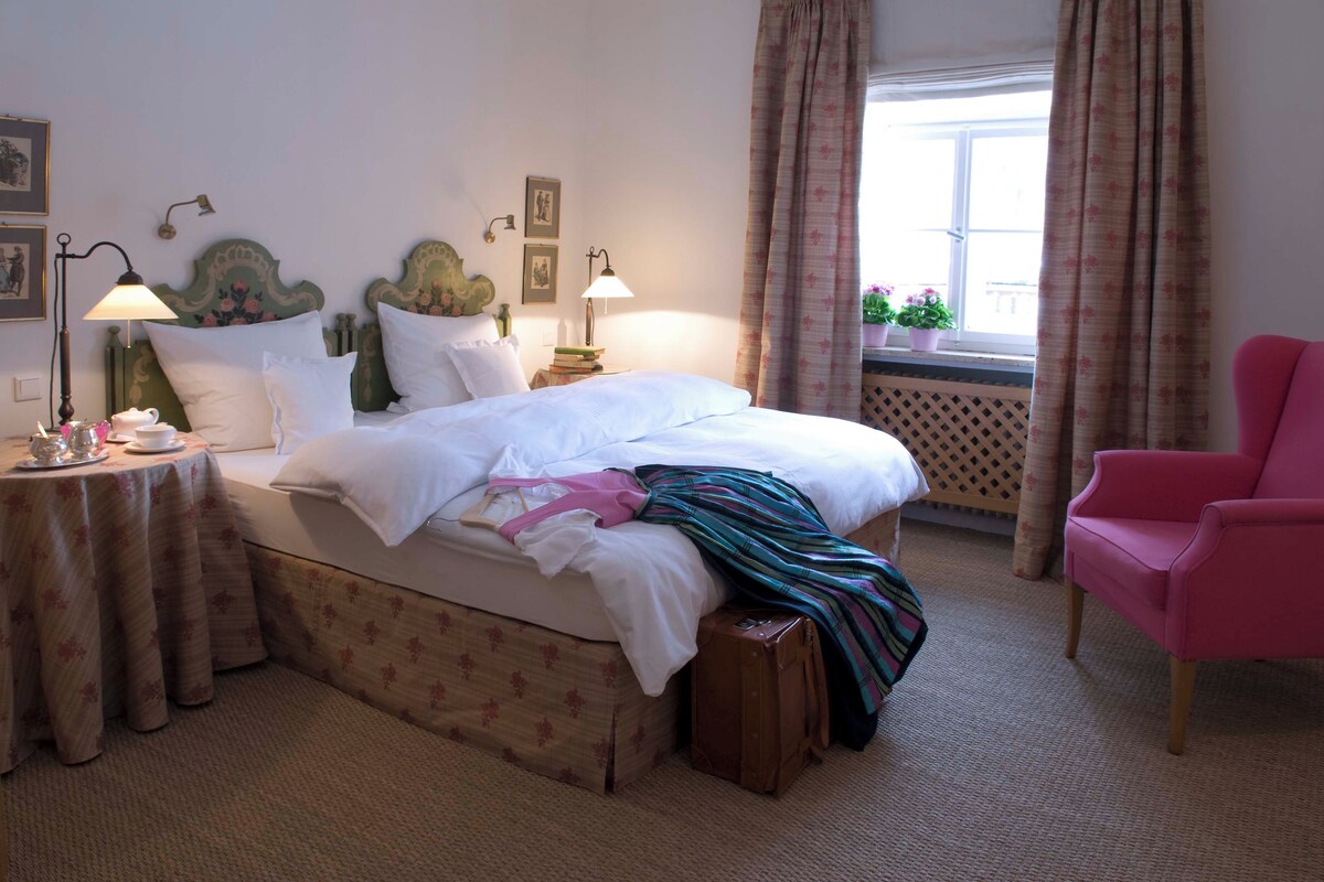A neatly arranged bedroom with a bed, bedside tables, a chair, and a window with curtains.