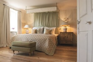 A bedroom with a bed, two bedside lamps, a wooden nightstand, a green upholstered bench, and a window with curtains. - Brauereigasthof-Hotel Aying (Aying)