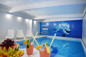 Zona de piscina con sillones de descanso, un bar junto a la piscina con frutas y bebidas, y un mural de una ballena.