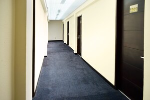 Un pasillo con pisos alfombrados, paredes color crema y puertas de madera oscura.