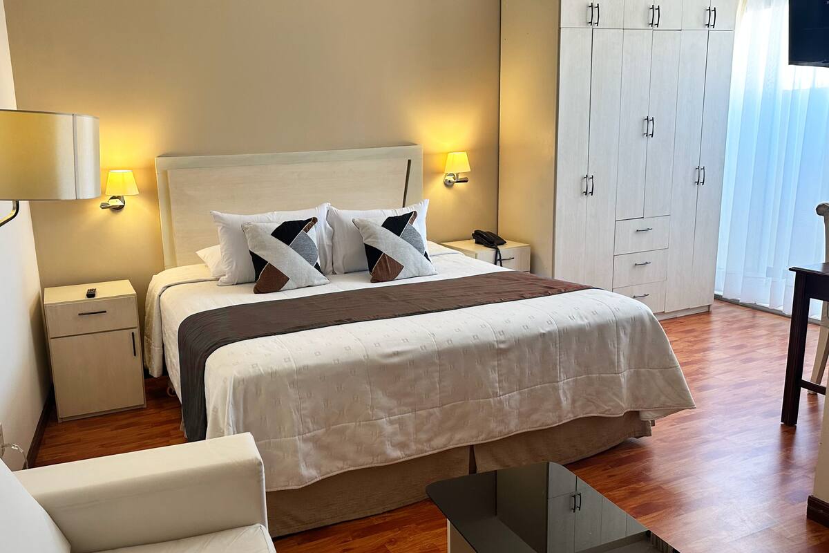 A hotel room with a bed, bedside tables, a lamp, a wardrobe, and a chair.