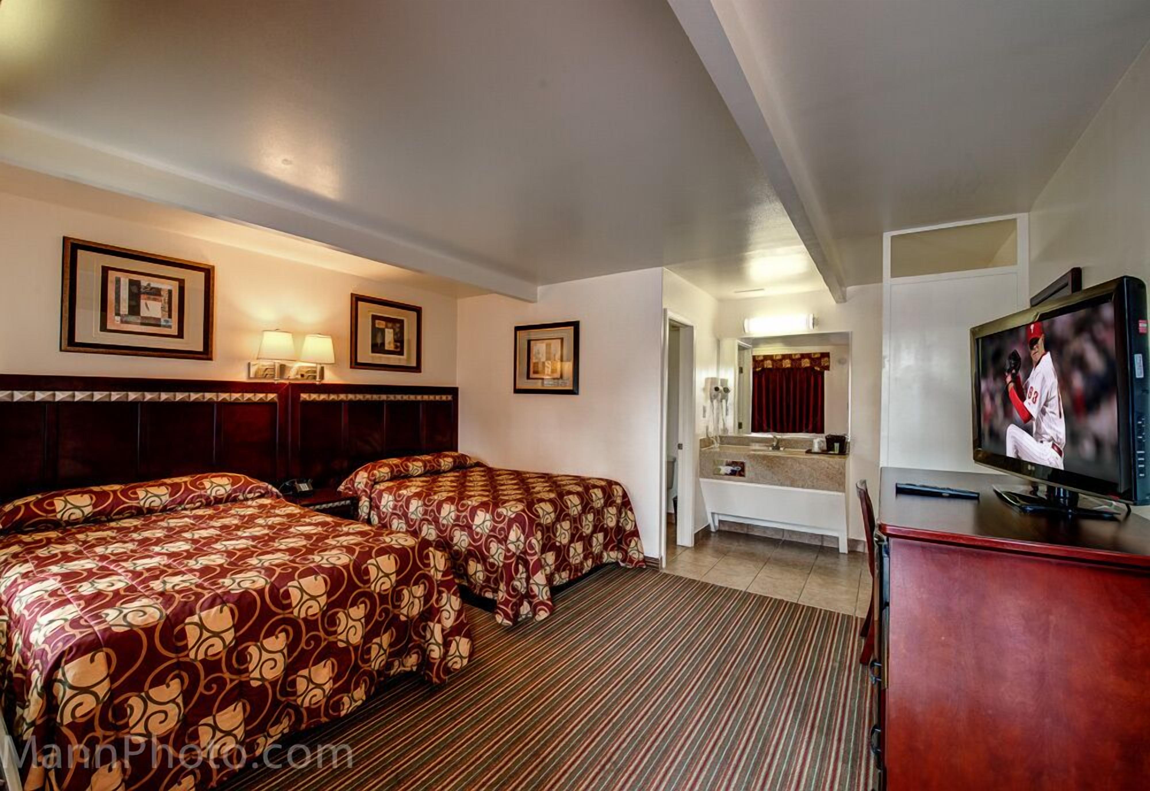 A hotel room with two beds, a TV, a desk, and a bathroom visible through an open door.