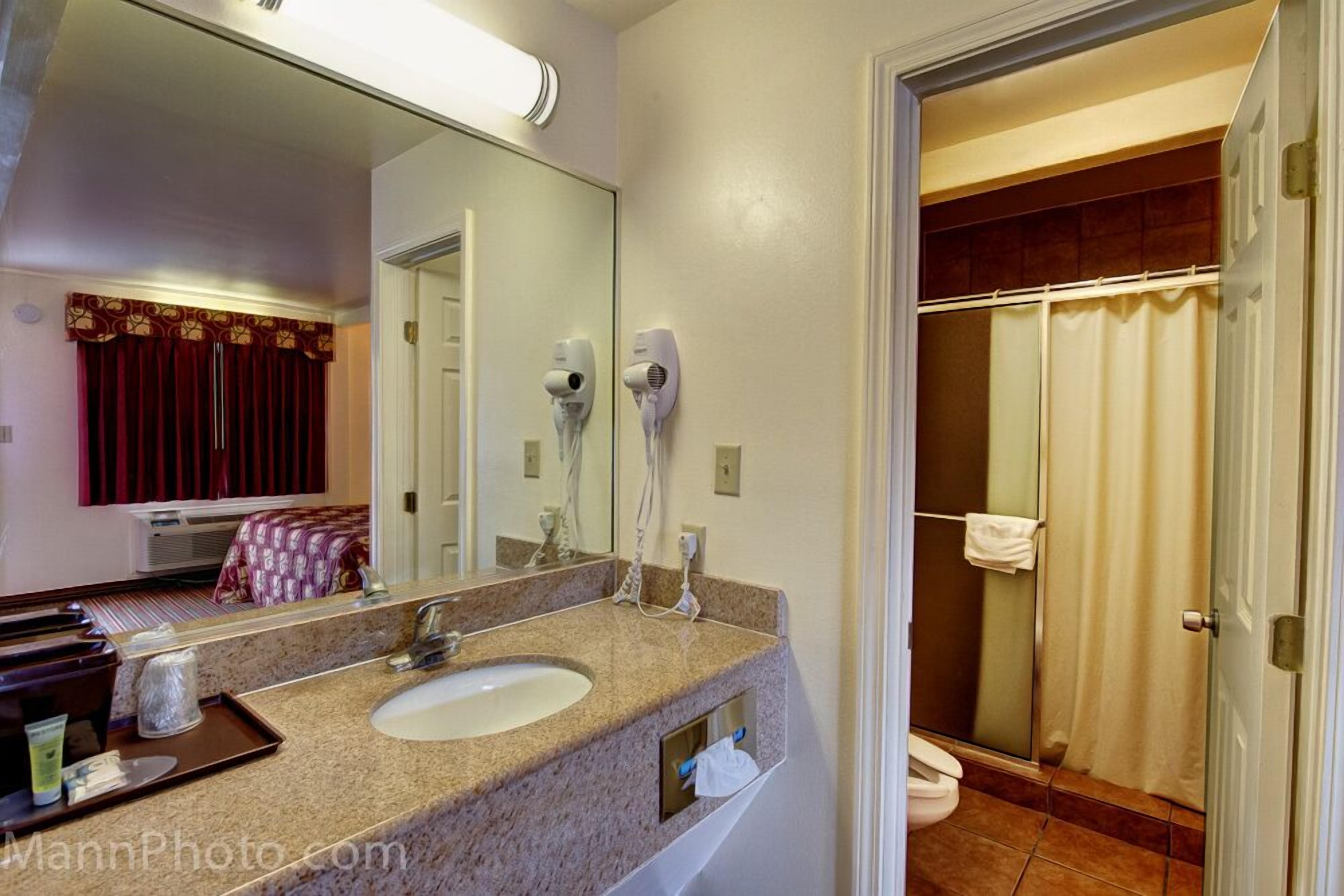 Une salle de bain d’hôtel équipée d’un lavabo, d’un miroir, d’un sèche-cheveux et d’une douche.