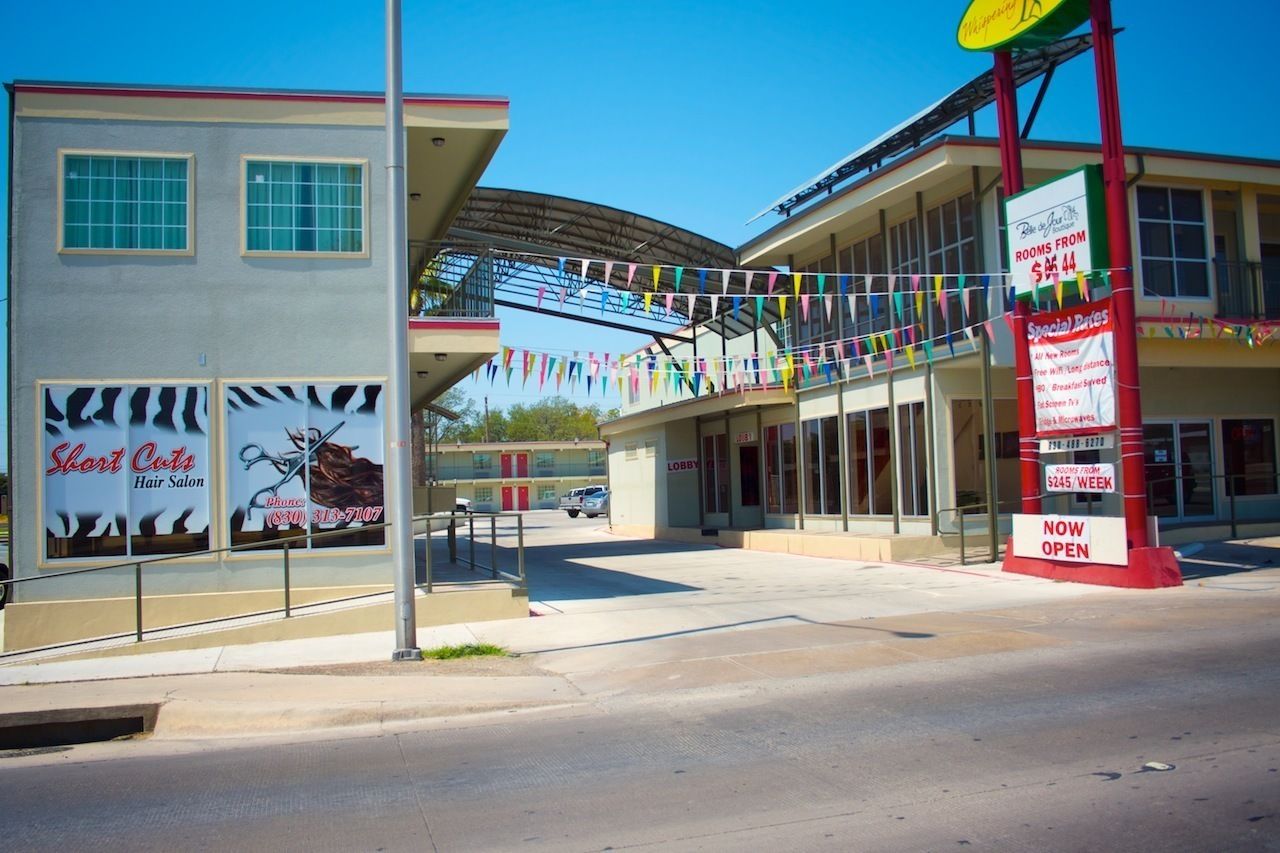 A building with a 'Short Cuts Hair Salon' sign, a 'Rooms from $44' sign, and a 'NOW OPEN' sign.