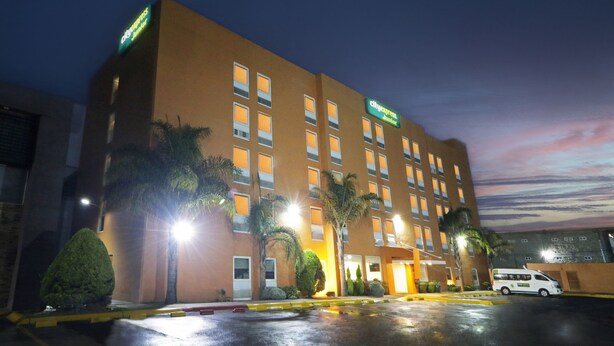 Un hotel de varios pisos con fachada plana, múltiples ventanas y un estacionamiento.