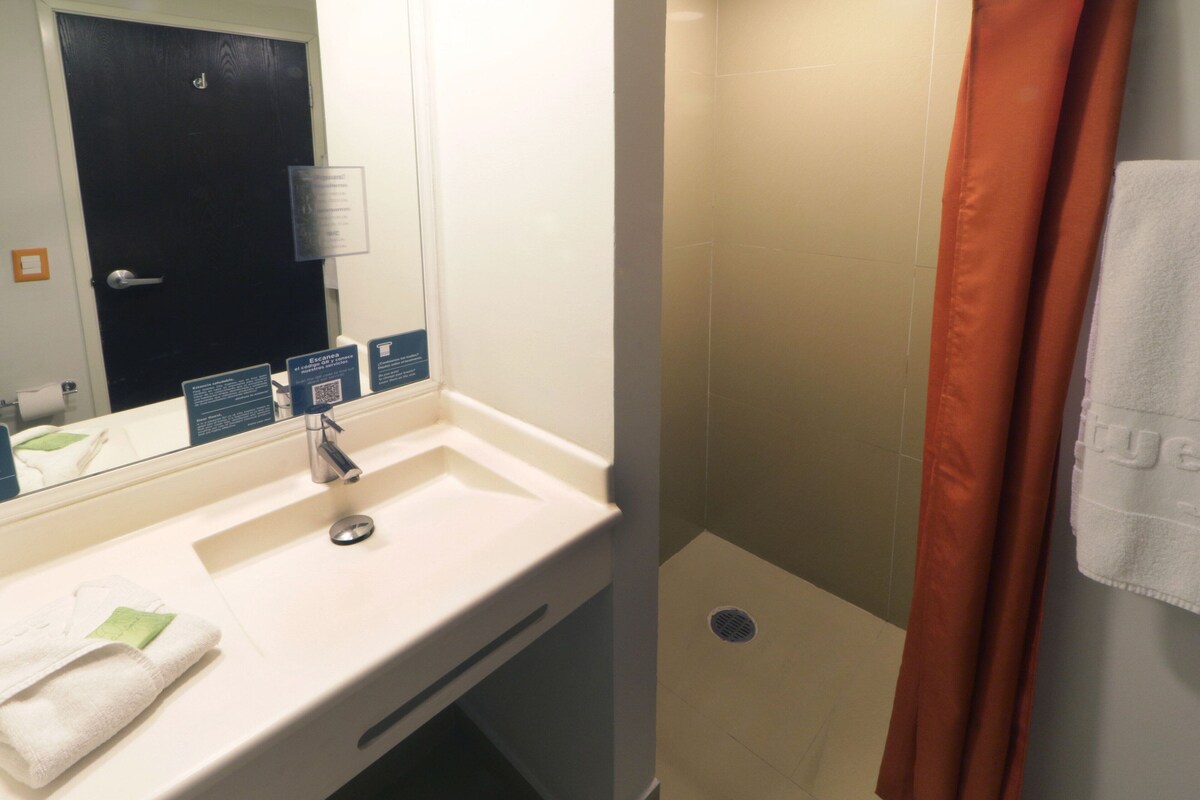 Une salle de bain avec un lavabo blanc, un miroir, une porte et un espace douche agrémenté d’un rideau de douche orange.