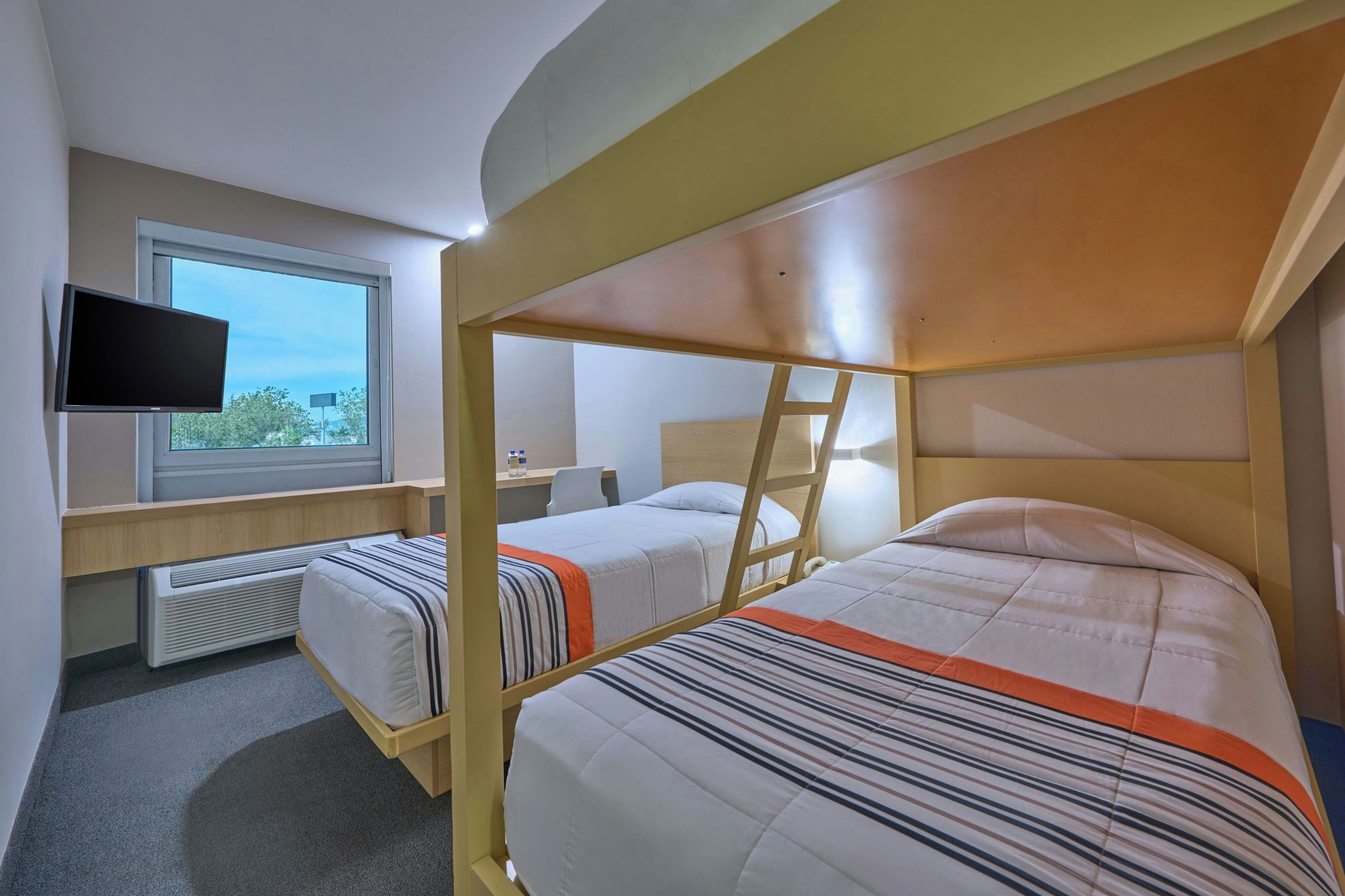 A bunk bed room with a television on the wall, a window, and a desk with a chair.