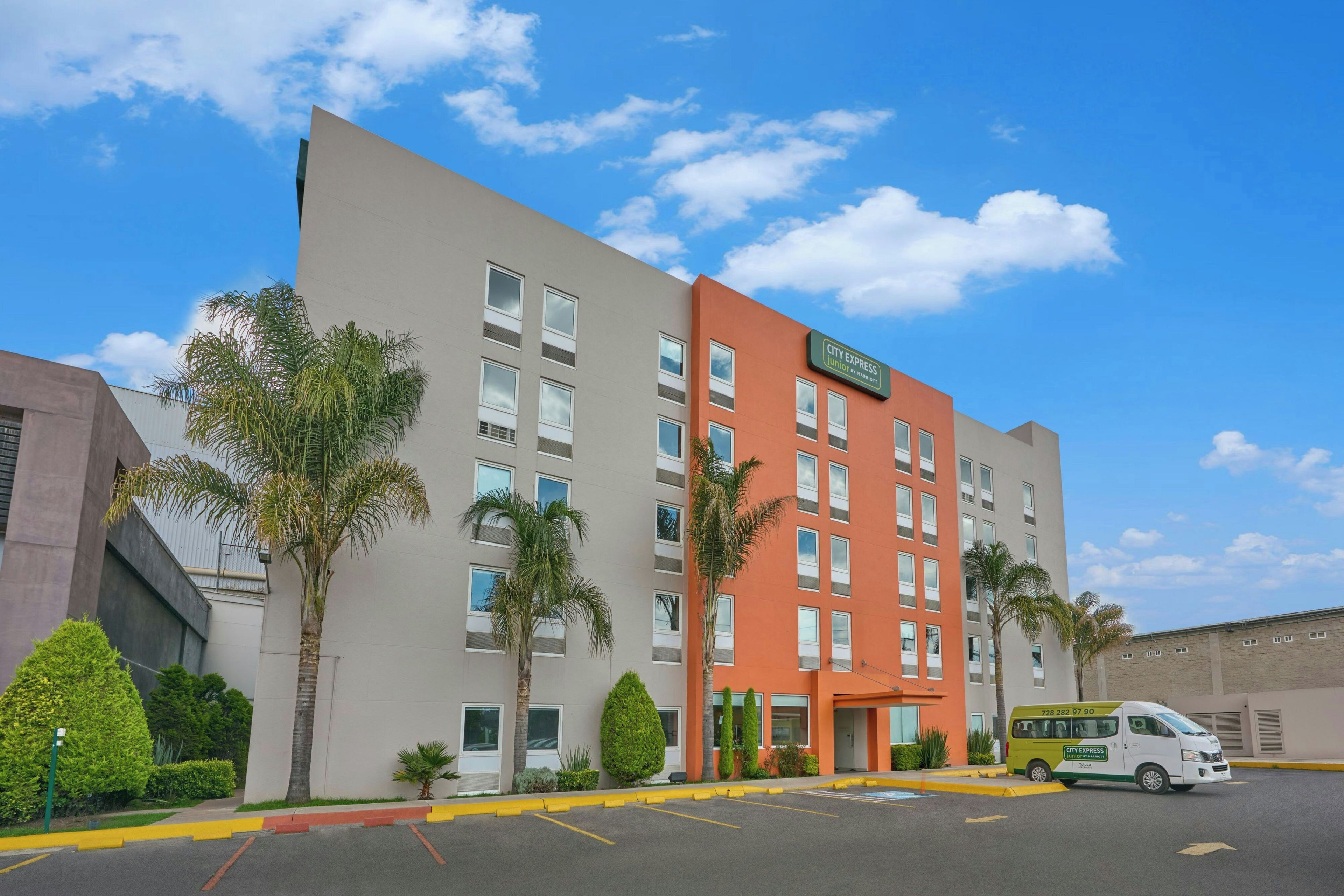 A multi-story hotel with a flat facade, a parking lot, and a City Express van parked in front.