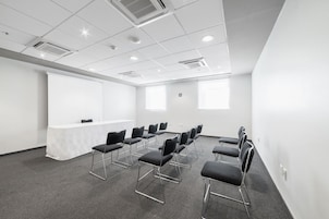 A conference room with a whiteboard, projector, and rows of black chairs.