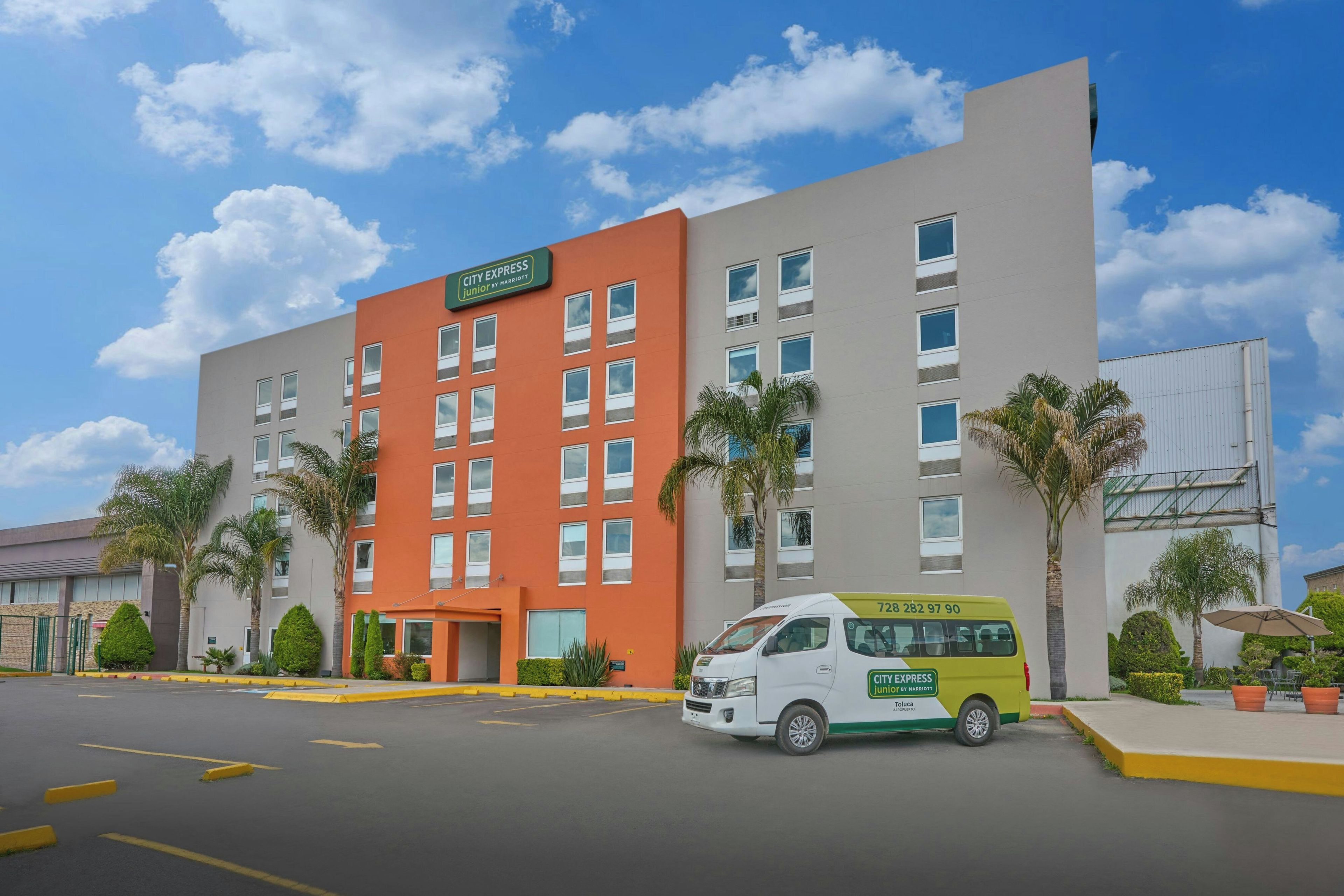 Un hotel City Express Junior by Marriott con un estacionamiento y una camioneta amarilla.