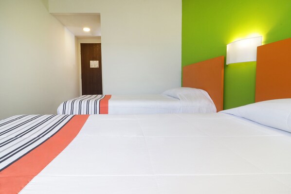 A hotel room with two beds, a green accent wall, and a white headboard.