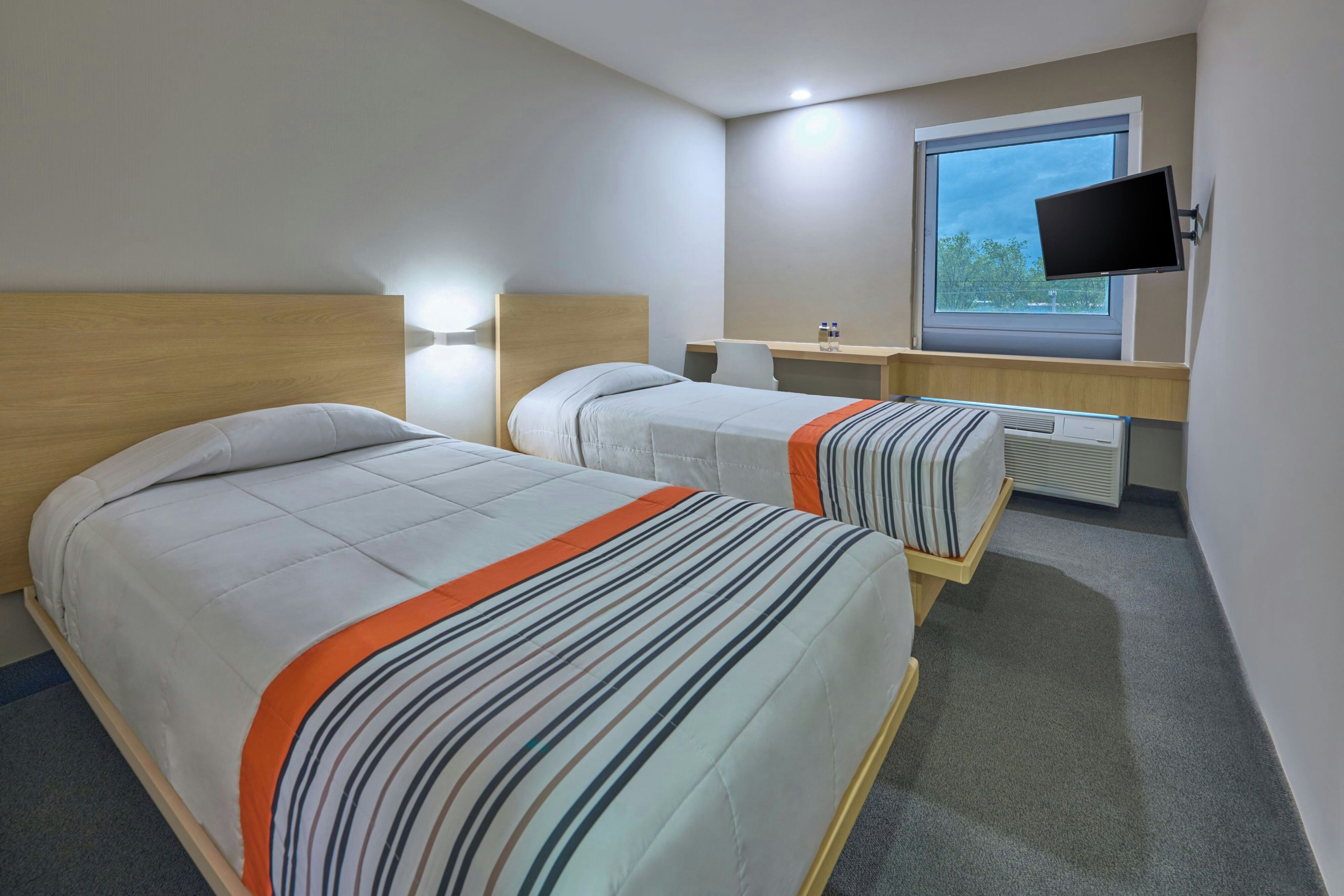 A hotel room with two beds, a desk, a TV, and a window.