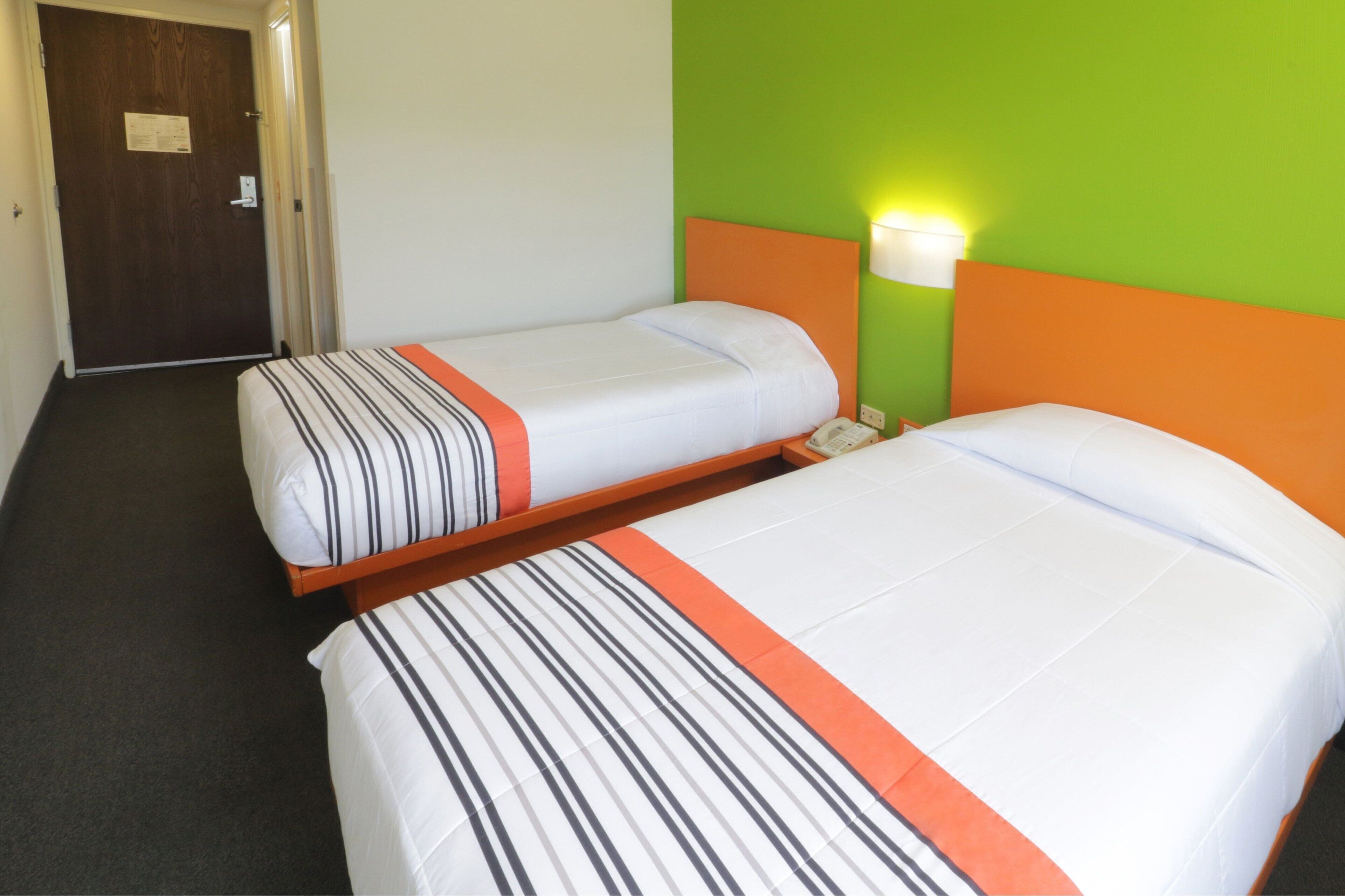 A hotel room with two single beds, each with striped bedding and an orange accent.