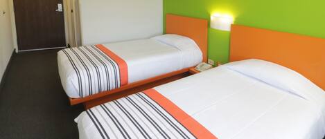 Una habitación de hotel con dos camas individuales, cada una con ropa de cama a rayas y un detalle naranja.