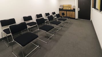 Un salón de conferencias con filas de sillas negras, un mostrador de madera con diversos objetos y una puerta.