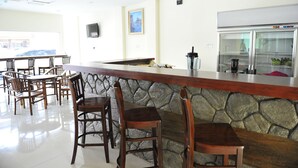 Un restaurante con pared de piedra, sillas de madera, mostrador y refrigerador.